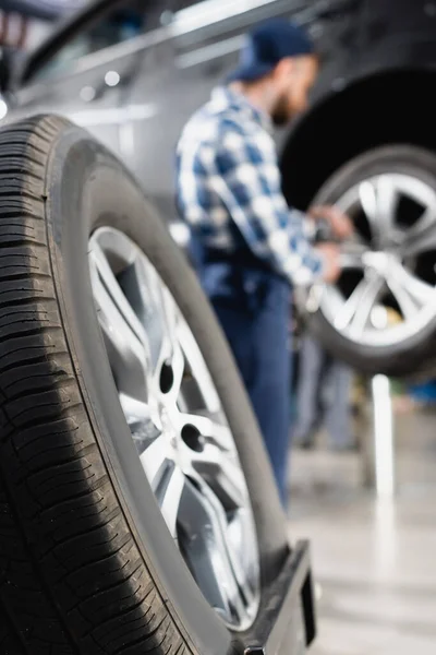 Vista de cerca de la rueda cerca del coche mecánico de reparación sobre fondo borroso - foto de stock