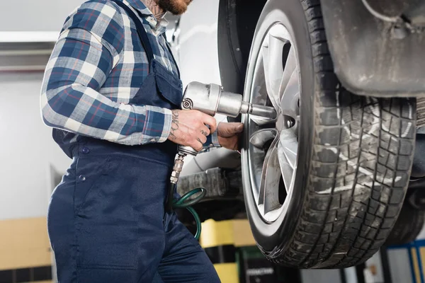 Cropped view of mechanic fixing wheel on car with pneumatic wrench — Stock Photo