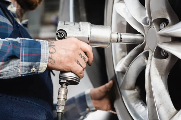 Cropped view of mechanic fixing car wheel with pneumatic wrench on blurred background — Stock Photo