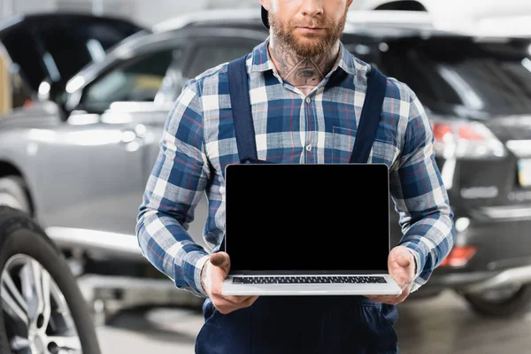 Vue recadrée du technicien tenant ordinateur portable avec écran blanc près de l'automobile sur fond flou — Photo de stock
