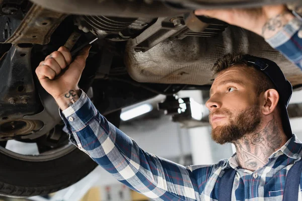 Young technician checking bottom of lifted car with wrench — Stock Photo