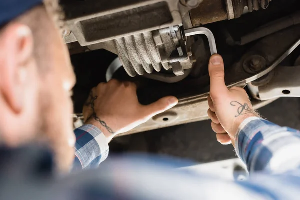 Mechanic repairing bottom of lifted car with wrench on blurred foreground — Stock Photo