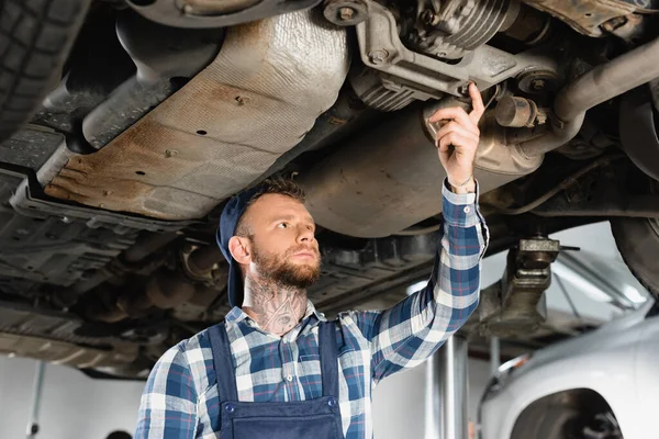 Jovem reparador fazendo diagnóstico de carro levantado a partir de baixo — Fotografia de Stock