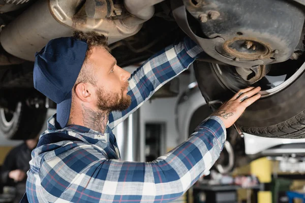 Young technician checking bottom of raised automobile in workshop — Stock Photo