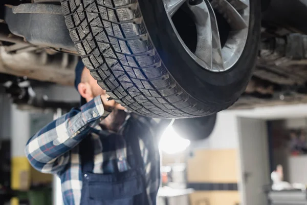 Cropped view of mechanic checking wheel under car on blurred background — Stock Photo