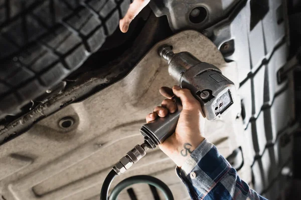 Cropped view of technician fixing detail of car with pneumatic wrench — Stock Photo