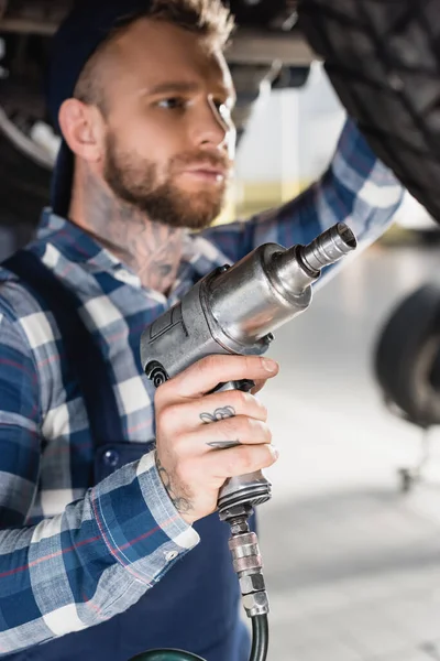 Reparaturarbeiter hält Druckluftschlüssel in Radnähe auf verschwommenem Hintergrund — Stockfoto