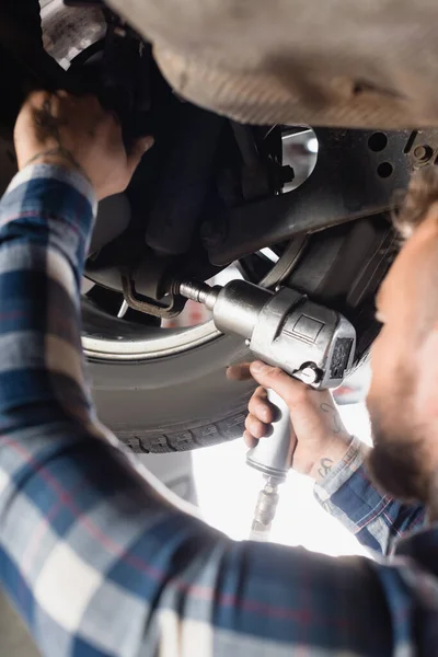 Teilansicht des Technikers, der das Autorad mit einem Druckluftschlüssel im unscharfen Vordergrund verstellt — Stockfoto