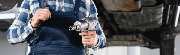 Cropped view of mechanic holding pneumatic wrench on blurred background, banner — Stock Photo