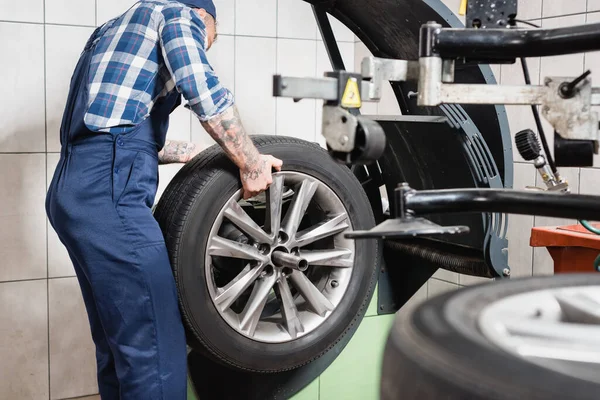 Cropped view of technician examining wheel on balance control machine in garage on blurred foreground — Stock Photo