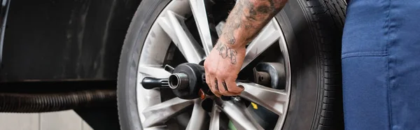 Partial view of tattooed mechanic adjusting car wheel, banner — Stock Photo