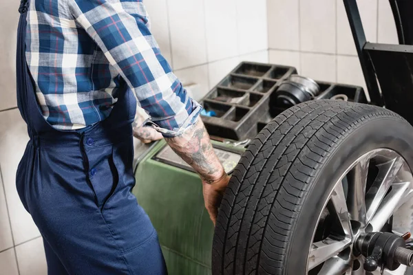 Partial view of mechanic checking wheel on balance control equipment in workshop — Stock Photo