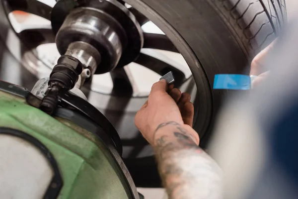 Partial view or repairman holding metallic balancing detail near wheel on blurred foreground — Stock Photo