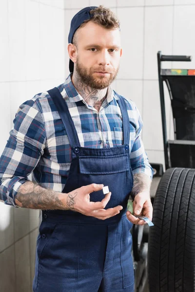 Young mechanic looking at camera while holding stripe of balancing plates near wheel — Stock Photo