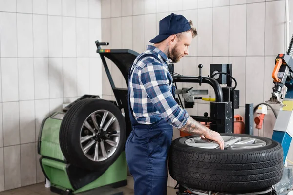 Reparador em macacão colocando roda na máquina de troca de pneus na oficina — Fotografia de Stock