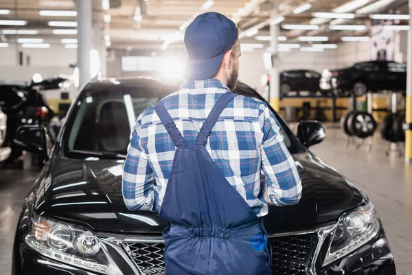 Vista trasera del mecánico en mono y la tapa de pie en el taller cerca de los coches — Stock Photo