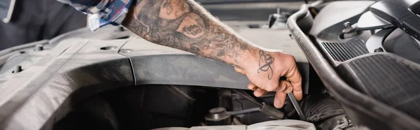 Vista recortada del técnico tatuado que comprueba el aceite del motor en el coche, bandera - foto de stock