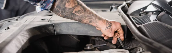Cropped view of tattooed technician checking engine oil in car, banner — Stock Photo