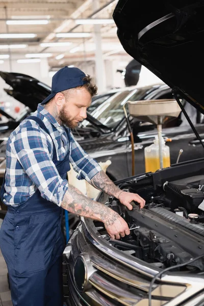 Joven técnico de limpieza del compartimiento del motor del coche en el taller - foto de stock