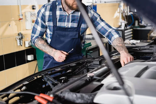 Partial view of tattooed technician examining car engine compartment on blurred foreground — Stock Photo