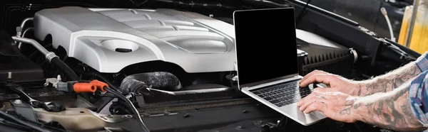 Cropped view of tattooed mechanic making car diagnostic on laptop near engine compartment, banner — Stock Photo