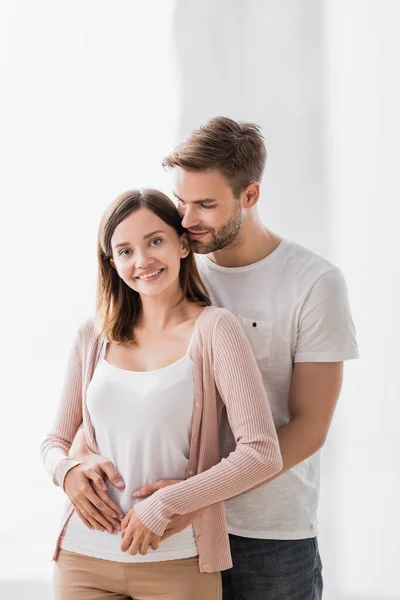 Mann umarmt fröhliche Freundin und schaut in Kamera — Stockfoto