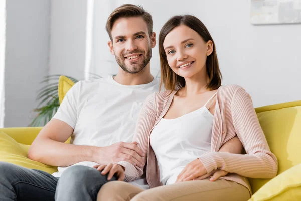 Fröhliche Männer und Frauen, die auf dem Sofa sitzen und zu Hause in die Kamera schauen — Stockfoto