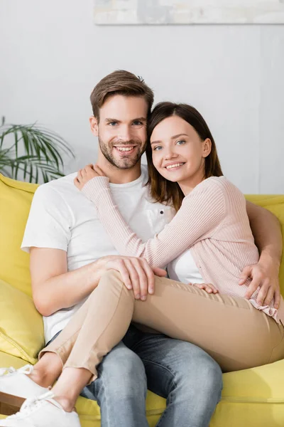 Cheerful man and woman hugging while sitting on sofa at home — Stock Photo