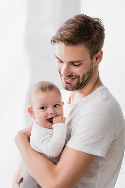 Happy father holding in arms baby boy sucking fingers — Stock Photo