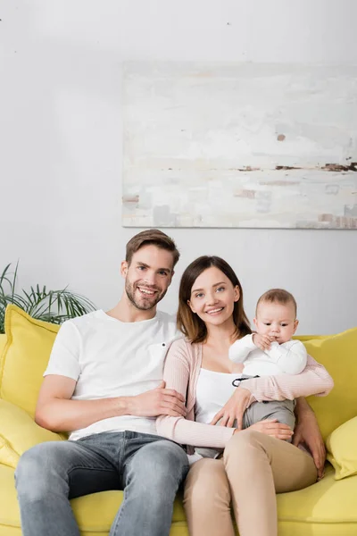 Pais felizes sorrindo perto do menino enquanto sentado no sofá — Fotografia de Stock