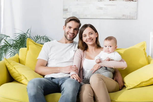 Padres alegres sonriendo cerca del niño mientras está sentado en el sofá - foto de stock