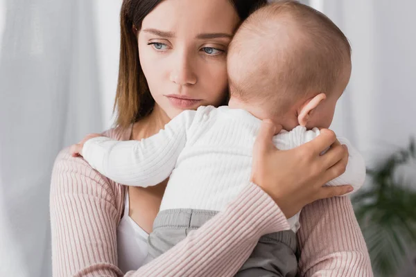 Madre preocupada sosteniendo en brazos bebé niño y mirando hacia otro lado - foto de stock