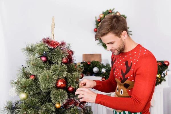 Hombre barbudo en jersey decorando árbol de navidad en casa - foto de stock