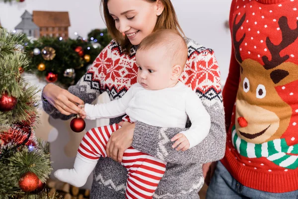 Mulher feliz segurando nos braços bebê menino enquanto decorando árvore de natal perto do marido — Fotografia de Stock