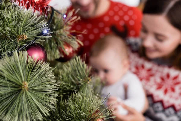 Árbol de Navidad decorado cerca de la familia borrosa en el fondo - foto de stock