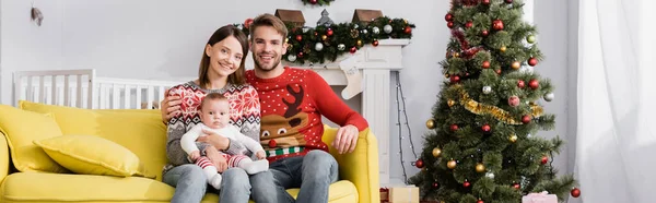 Famille heureuse avec bébé garçon assis sur le canapé près de l'arbre de Noël, bannière — Photo de stock