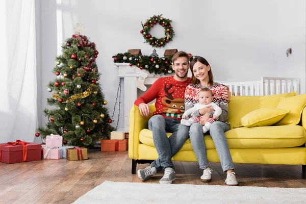 Familia feliz con bebé niño sentado en el sofá cerca del árbol de Navidad - foto de stock