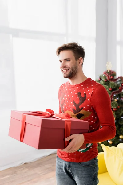 Happy man in red sweater holding wrapped christmas present — Stock Photo