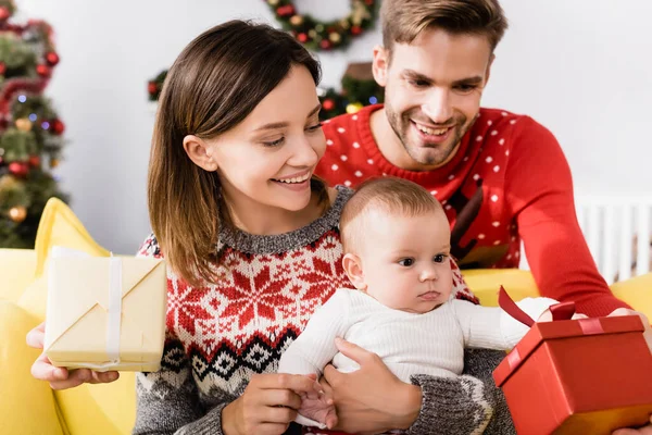 Glückliche Eltern mit verpackten Weihnachtsgeschenken in der Nähe ihres kleinen Sohnes — Stockfoto