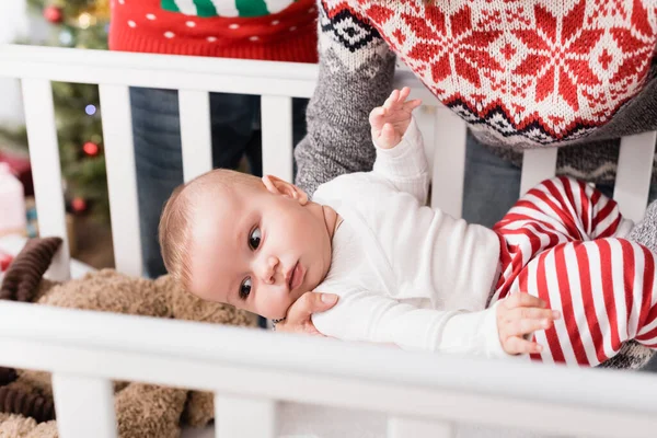 Mère tenant dans les bras bébé garçon près de la crèche tout en se tenant avec mari — Photo de stock