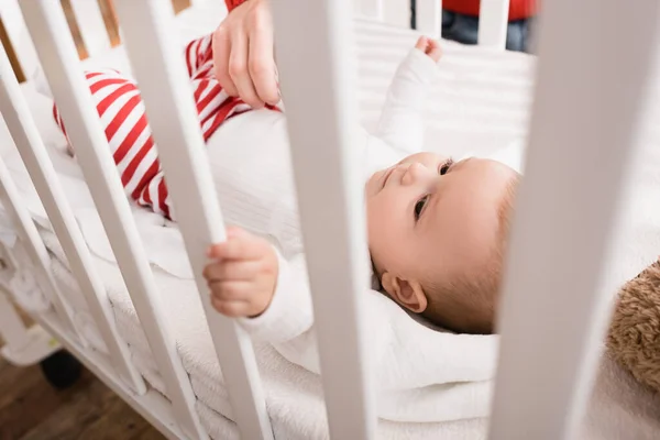 Рука отца рядом с младенцем-сыном в детской кроватке на размытом переднем плане — стоковое фото