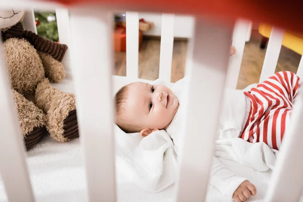 Infant boy lying in baby crib on blurred foreground — Stock Photo