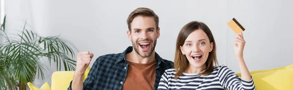 Happy woman holding credit card near excited husband, banner — Stock Photo