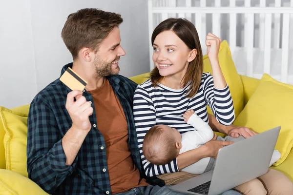 Homem alegre segurando cartão de crédito perto da esposa animado com o filho infantil enquanto compras on-line — Fotografia de Stock