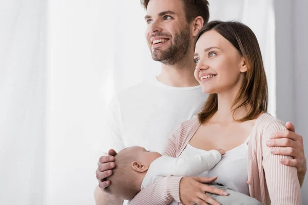 Улыбающаяся женщина, держащая в руках младенца, рядом с веселым мужем — стоковое фото