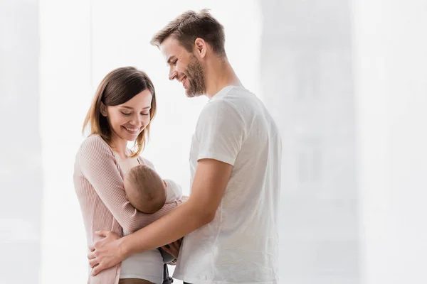 Fürsorgliche Frau hält Säugling neben fröhlichem Ehemann im Arm — Stockfoto