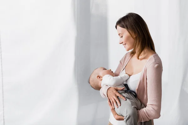 Caring woman smiling while holding in arms infant boy — Stock Photo