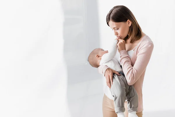 Madre che tiene in braccio bambino e bacia mano minuscola — Foto stock