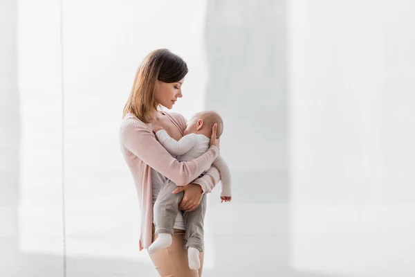 Joven madre sosteniendo en brazos somnoliento bebé hijo - foto de stock