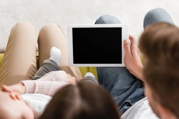 Vista superior de la tableta digital con pantalla en blanco en la mano del hombre cerca de esposa feliz sosteniendo en brazos hijo lactante en primer plano borroso - foto de stock